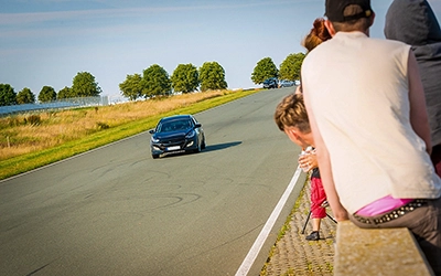 Ein dunkler Hyundai beschleunigt auf einer Rennstrecke, mit Zuschauern im Vordergrund, die das Viertelmeilenrennen verfolgen.